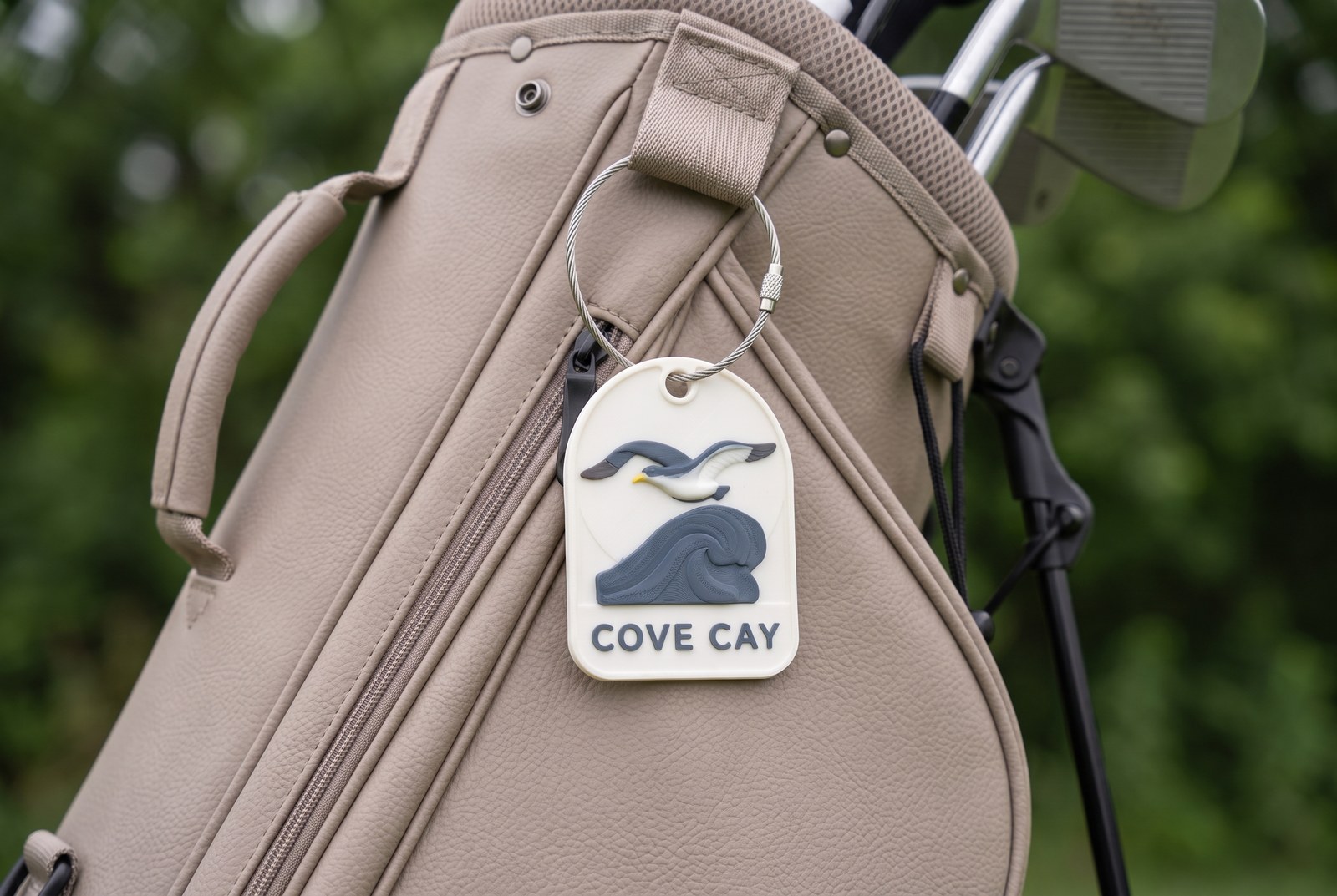 Cove Cay bag tag — bone-white arched tag with a slate-blue seagull over a wave, hung from a golf bag on a steel cable